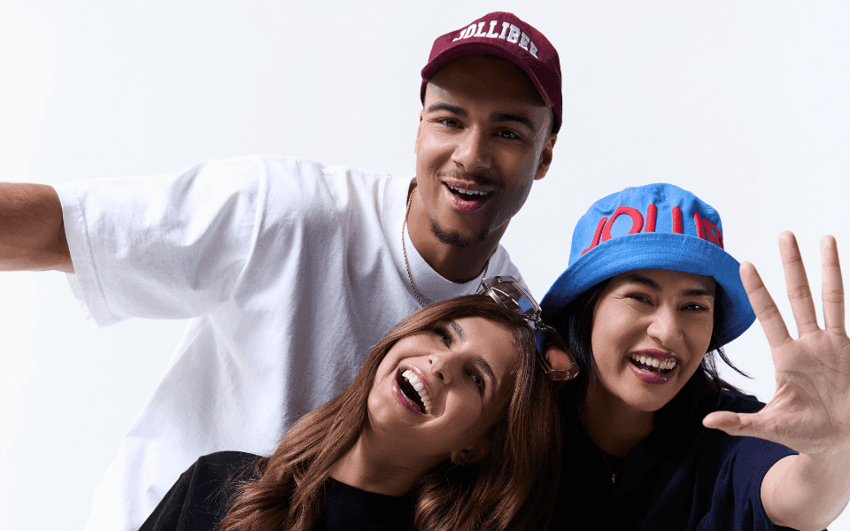 Three people wearing Jollibee branded hats having fun on a white background.