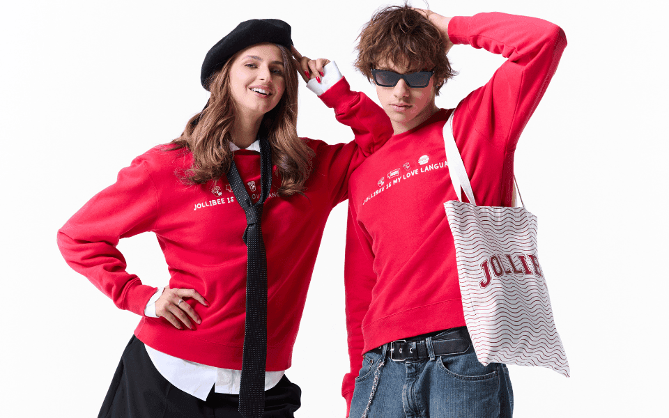 Two people wearing matching Jollibee sweatshirts on a white background